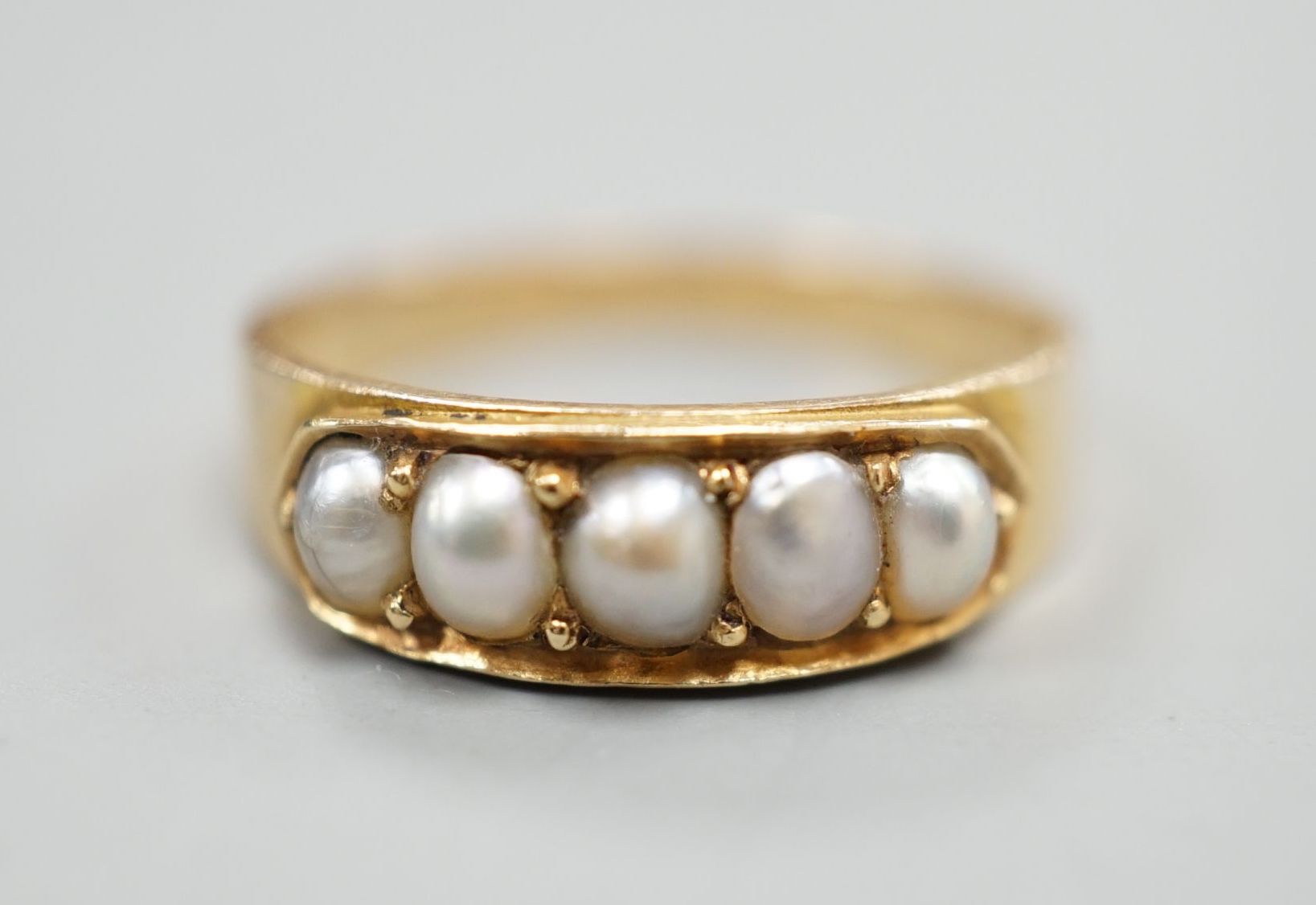 A yellow metal and graduated five stone split pearl set half hoop ring, size M, gross 3 grams.